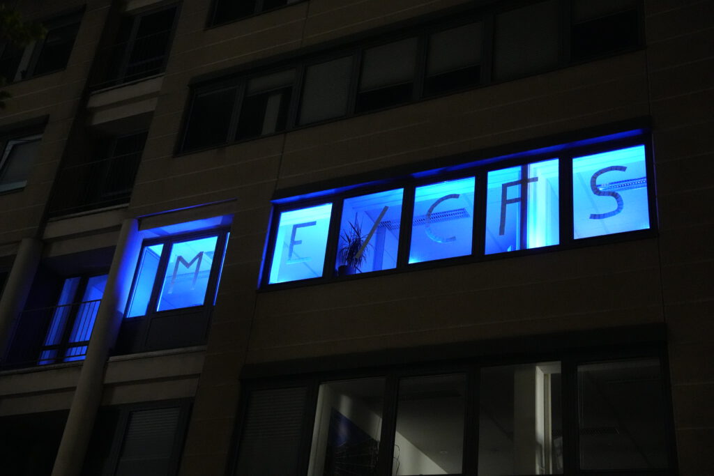 ideenhunger Büro bei Nacht mit blau beleuchteten Fenstern, in denen die Buchstaben ‚M E / C F S‘ zu sehen sind.