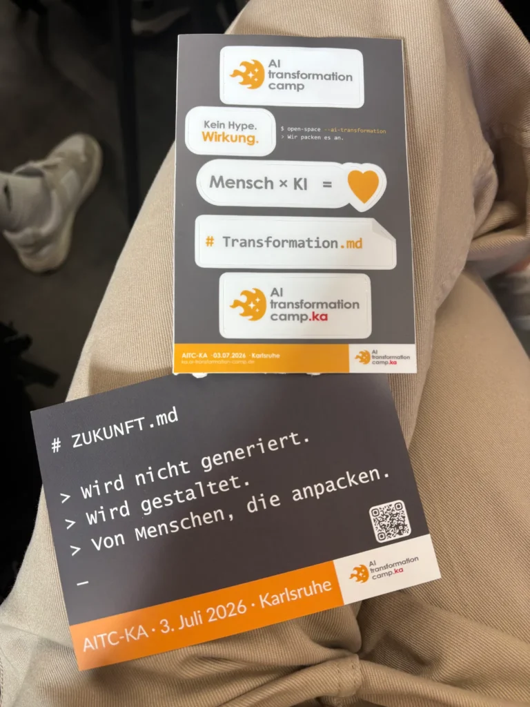 Gedruckte Karten und Flyer des AI Transformation Camps liegen auf einem Schoß. Auf einer Karte steht: „Zukunft wird nicht generiert. Wird gestaltet. Von Menschen, die anpacken.“