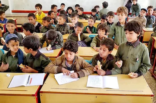 Mehrere Kinder sitzen gemeinsam in Jemen in einem Klassenraum an Schultischen und schreiben in ihre Hefte. 