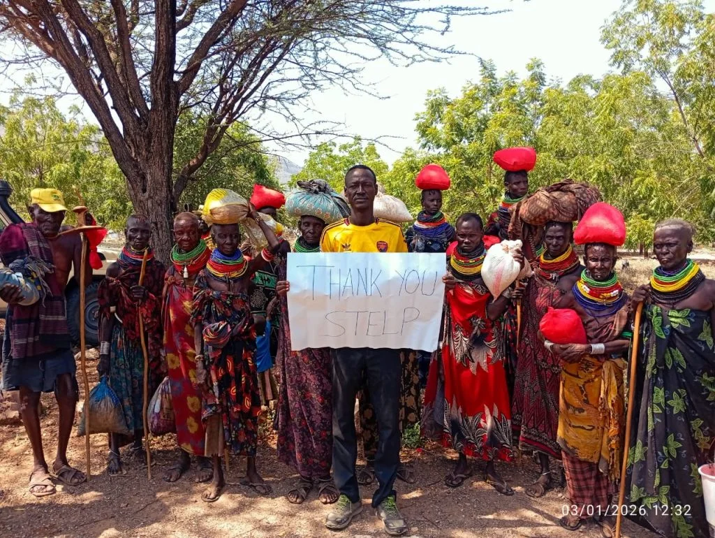 Eine Gruppe von Kindern und Erwachsenen steht im Freien in Kenia zusammen und hält ein Schild in die Kamera auf dem steht: "THANK YOU STELP".