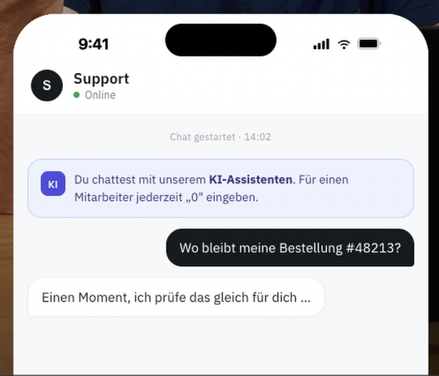 Auf einem Smartphone ist ein Support-Chat zu sehen. Ein Hinweis informiert darüber, dass die Kommunikation mit einem KI-Assistenten erfolgt und jederzeit ein menschlicher Mitarbeiter angefordert werden kann. Der Nutzer fragt nach dem Status seiner Bestellung.