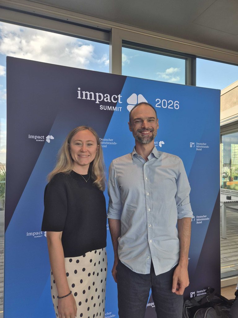 Benjamin und Elisa vor der impact SUMMIT Social Media-Wand für ein Erinnerungsfoto.