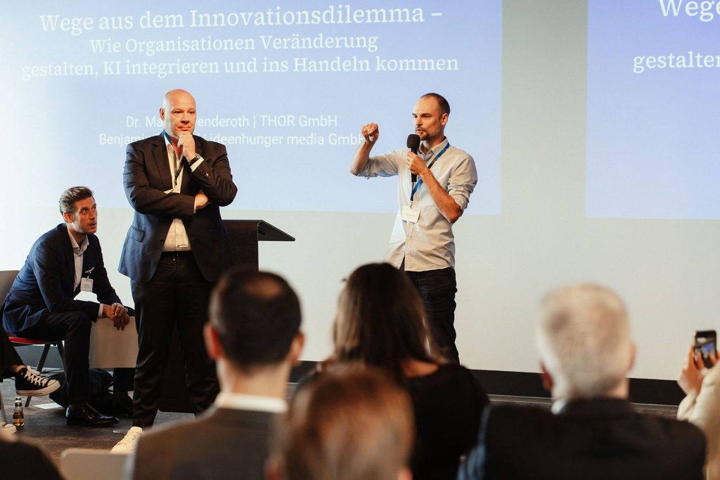 Benjamin Burkard und Martin Wenderoth stehen auf der Bühne des impact SUMMIT und halten einen Impulsdialog ab. 